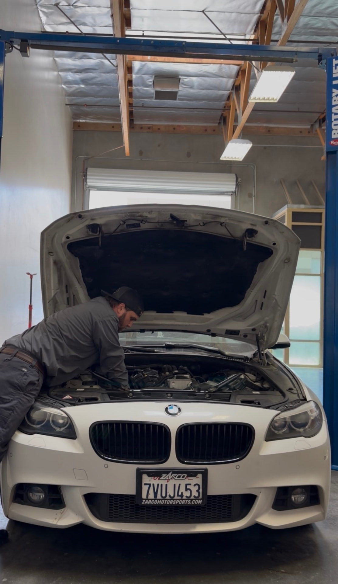 Mechanic inspecting the engine of a BMW under a hydraulic lift at Johnny's Auto Repair on Ridgecrest Road in Victorville CA