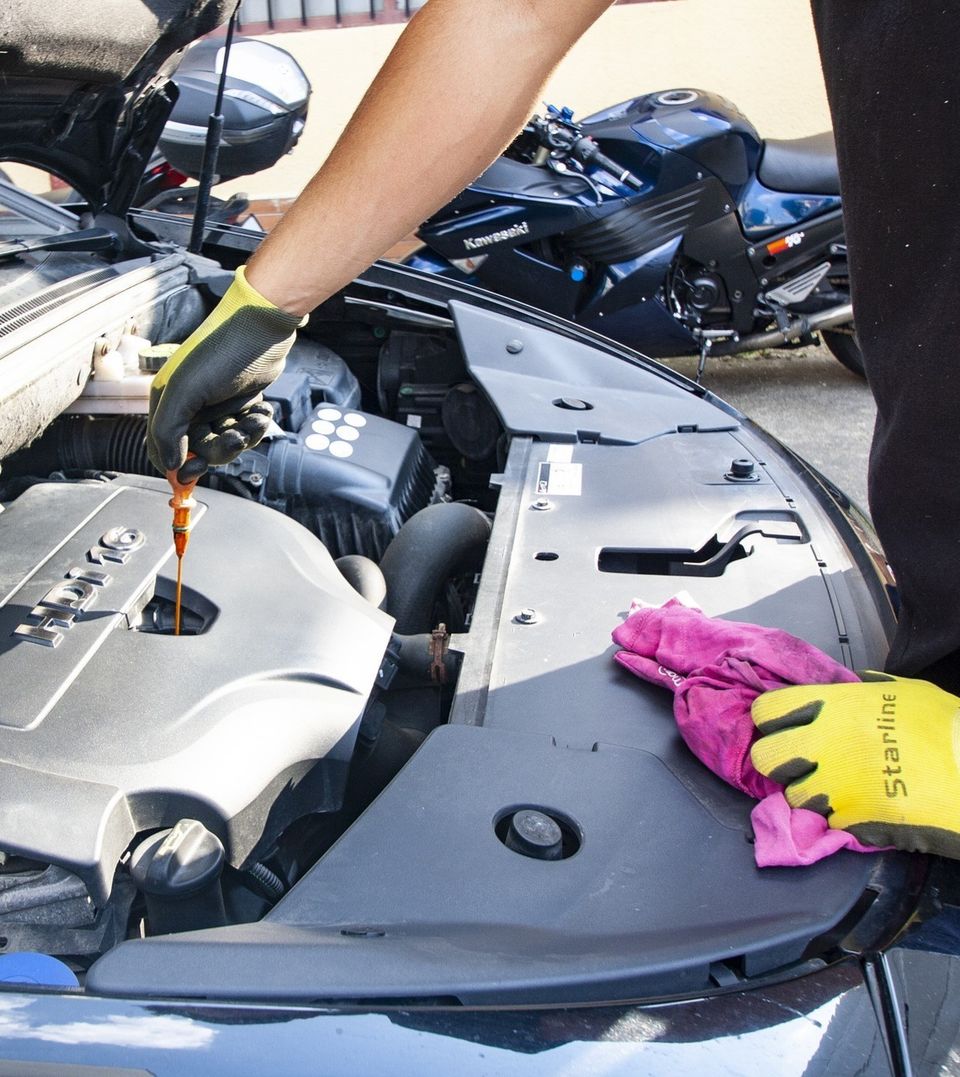 Gloved hands checking engine oil with the dipstick during an oil change at Johnny's Radiator and Auto Repair