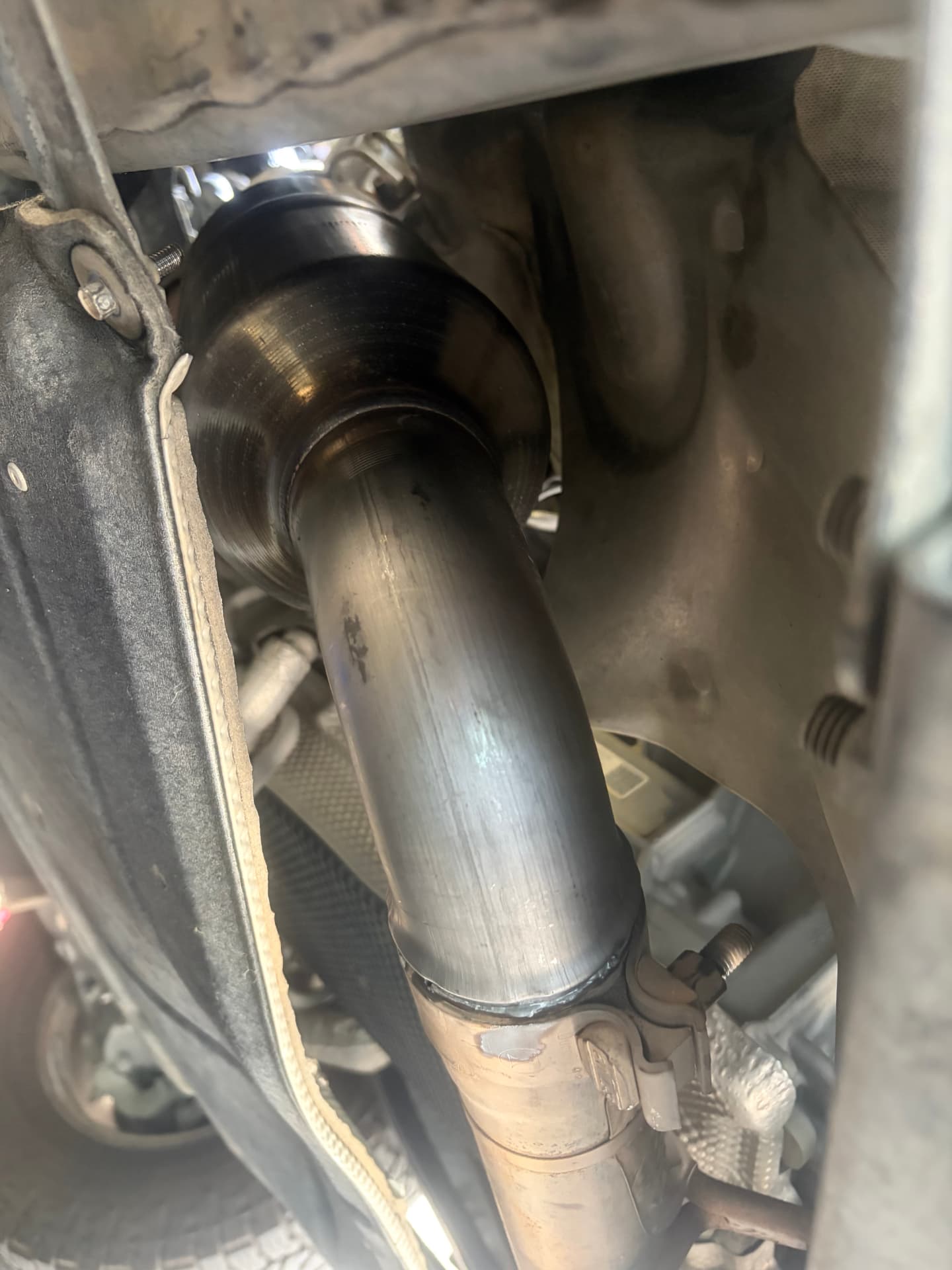 Newly installed exhaust pipe section viewed from under a vehicle at Johnny's Auto Repair in Victorville CA