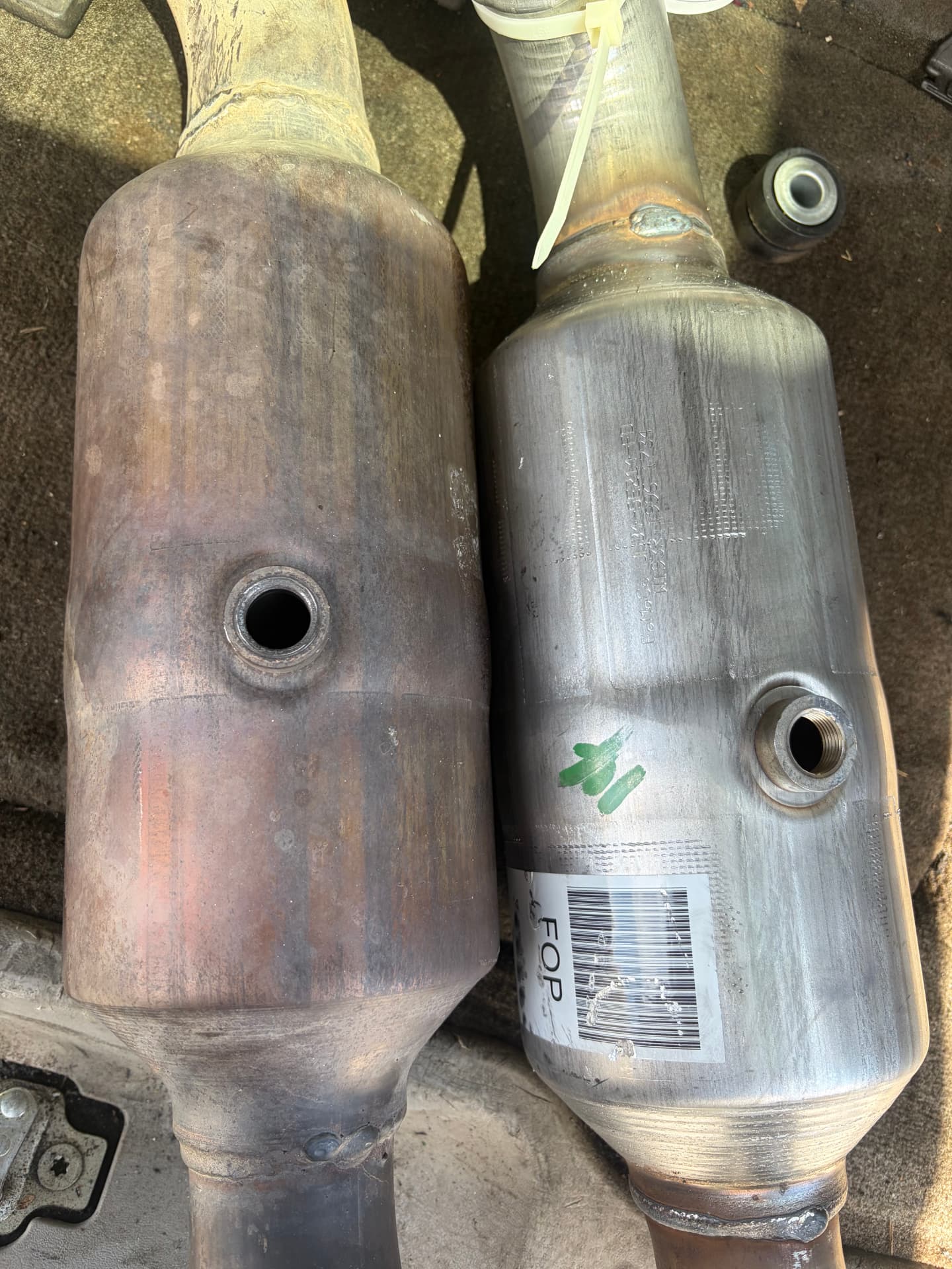 Old rusted catalytic converter next to a new replacement on the shop floor at Johnny's Auto Repair in Victorville CA