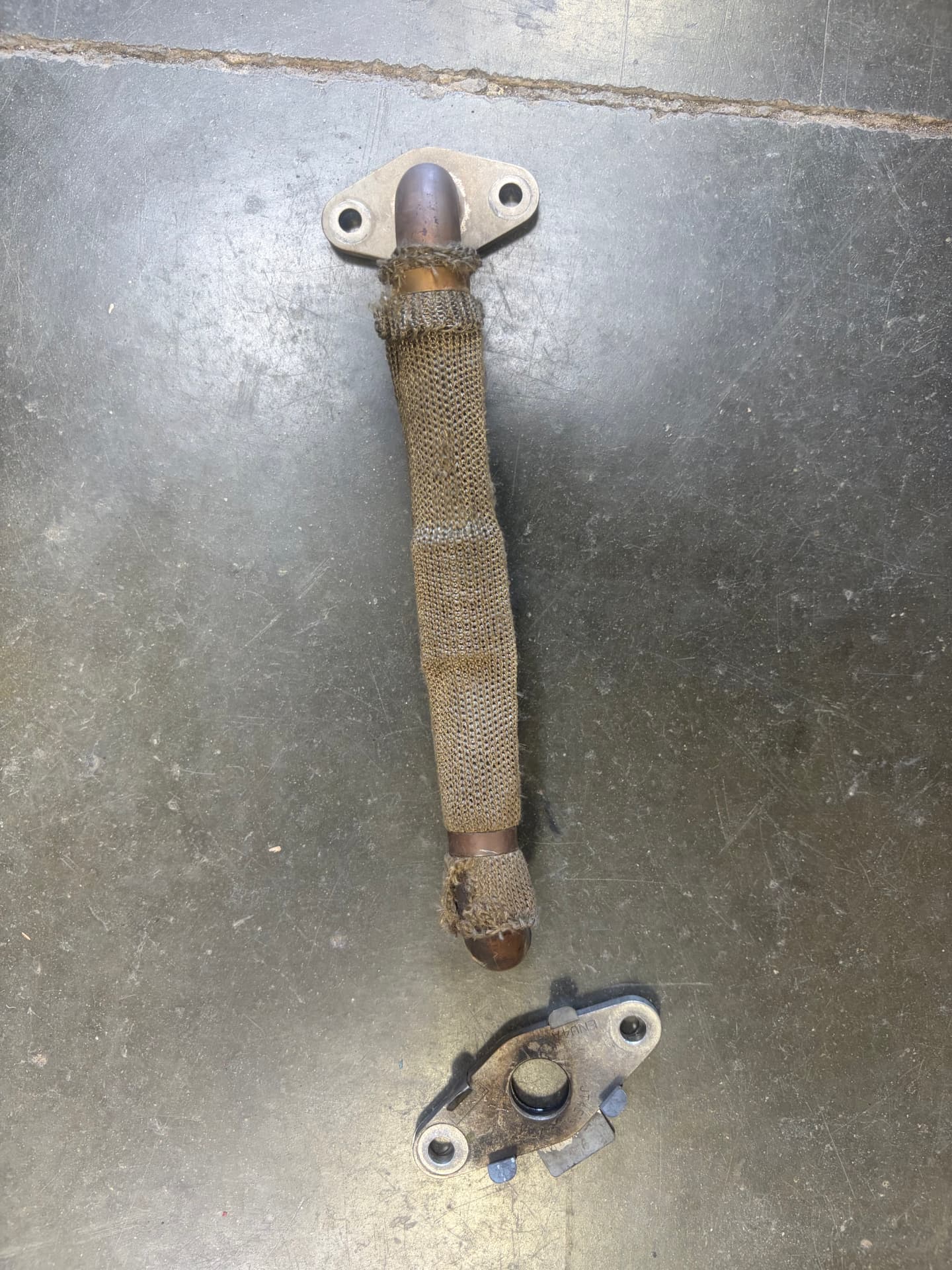 Exhaust pipe with woven heat sleeve and mounting flange on the shop floor at Johnny's Auto Repair in Victorville CA